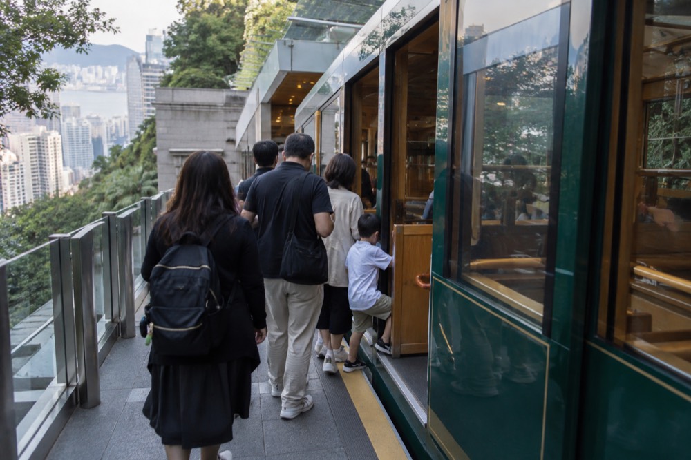Passengers boarding a green Peak Tram funicular car at a platform