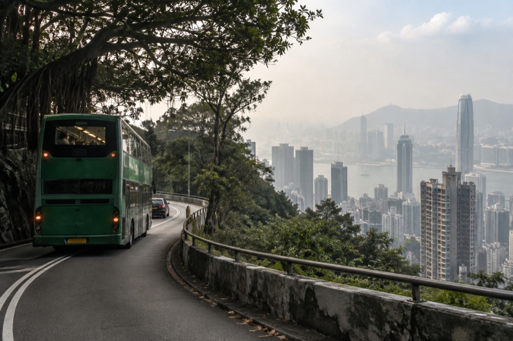 A green Citybus double decker on the winding road up to the Peak with the city skyline below