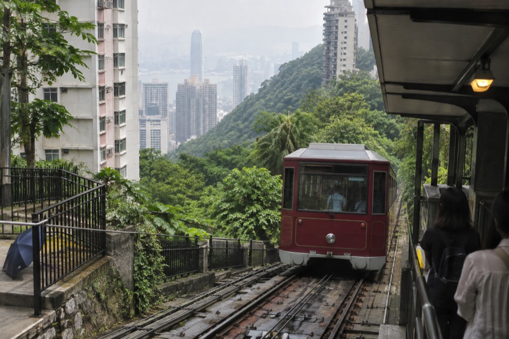 Peak Tram car on steep track passing apartment towers on the forested hillside