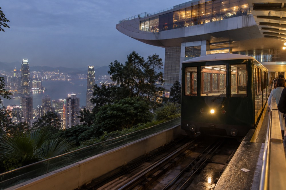 Green Peak Tram car arriving at the upper terminus beside the Peak Tower at dusk