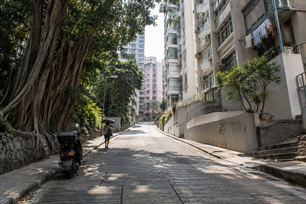 A steep narrow road rising between apartment towers and trees on Hong Kong Island