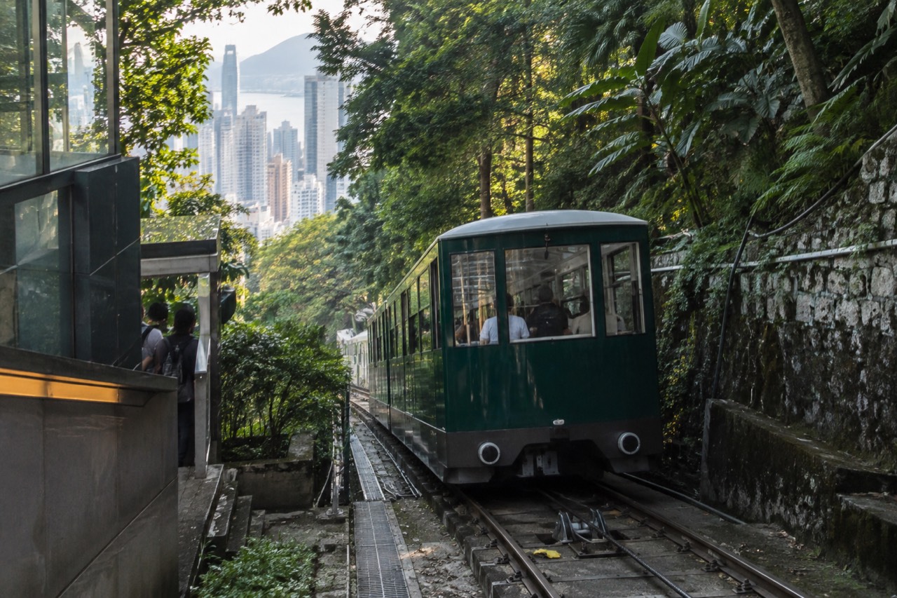 Green Peak Tram funicular car climbing the forested hillside above Hong Kong towers