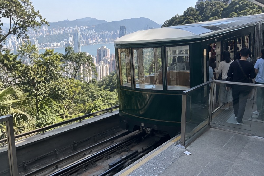 A green funicular car at the upper station with passengers boarding
