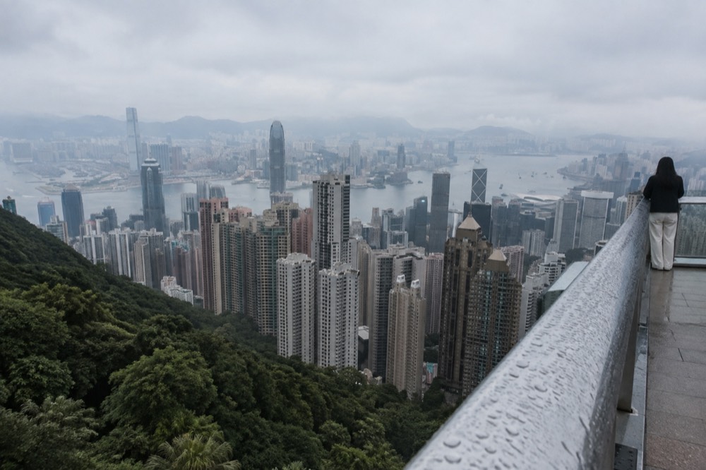 A rooftop viewing platform railing with city towers and a harbour beyond