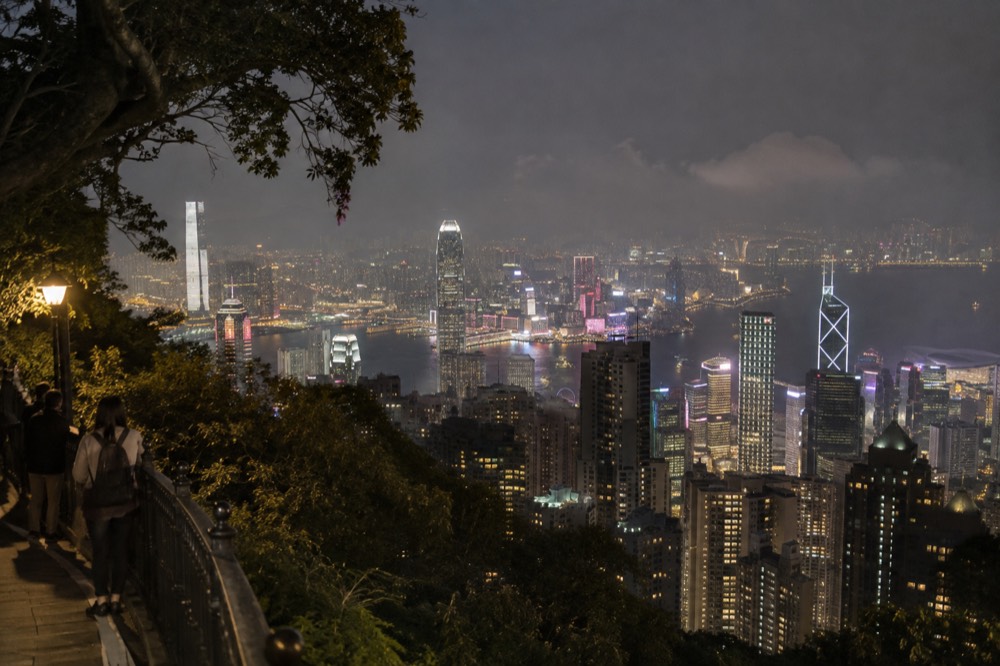 Night view over Victoria Harbour and the Kowloon skyline from an elevated hillside path