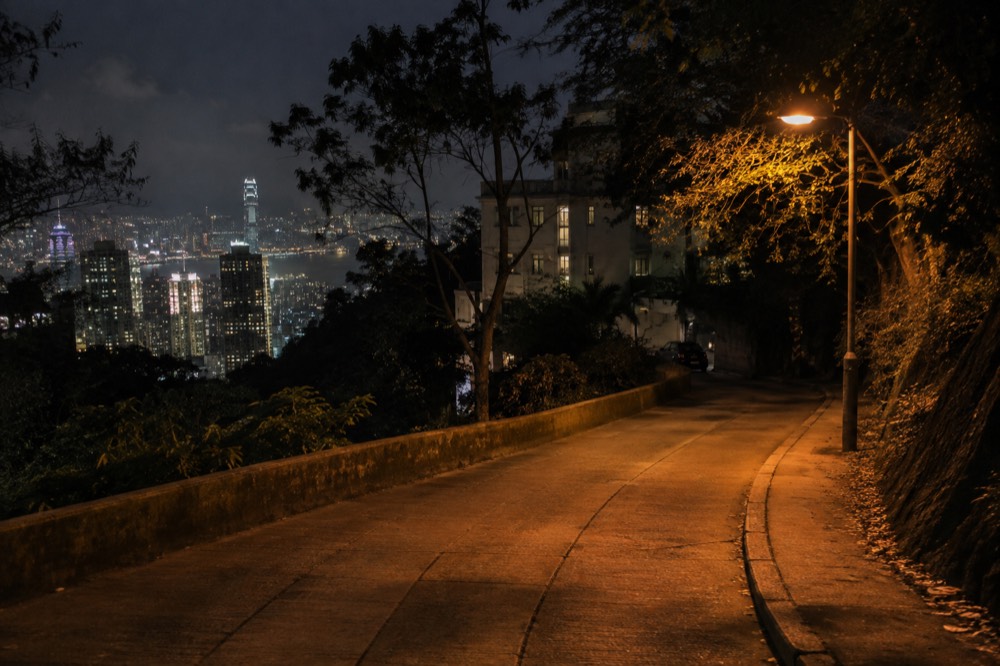 City lights of Hong Kong Island stretching below a dark hillside road at night