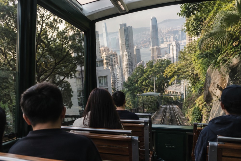 The interior of a modern Peak Tram car with tiered seats and large panoramic windows looking over the city