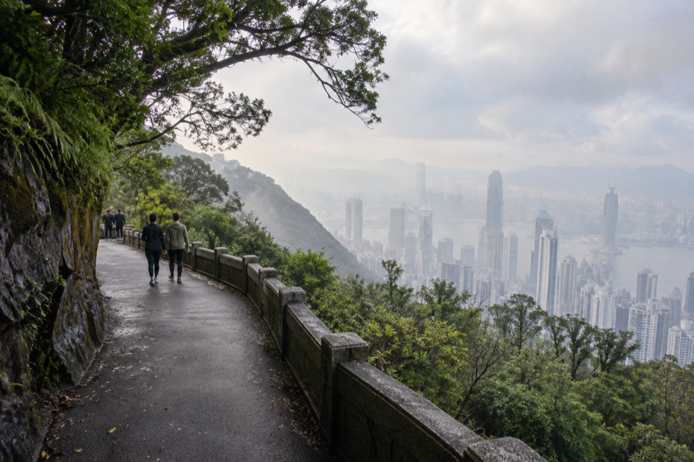 A narrow road on a green hillside with apartment towers visible far below
