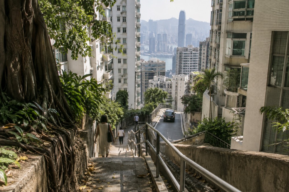 A steep narrow road descending between residential towers with a hazy skyline beyond