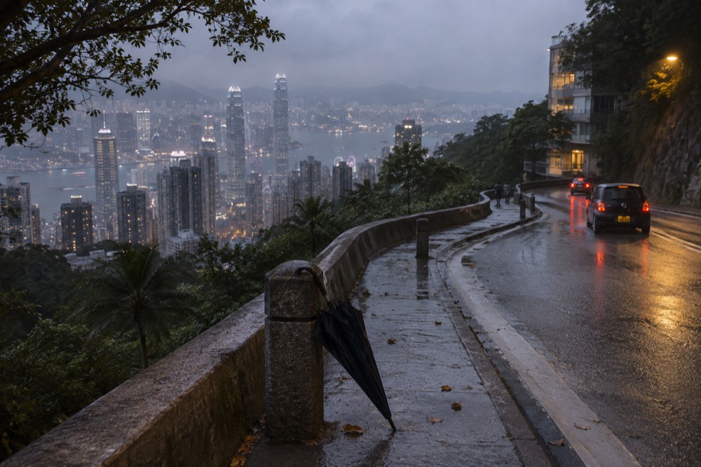 A winding hillside road at dusk with city lights beginning to appear below
