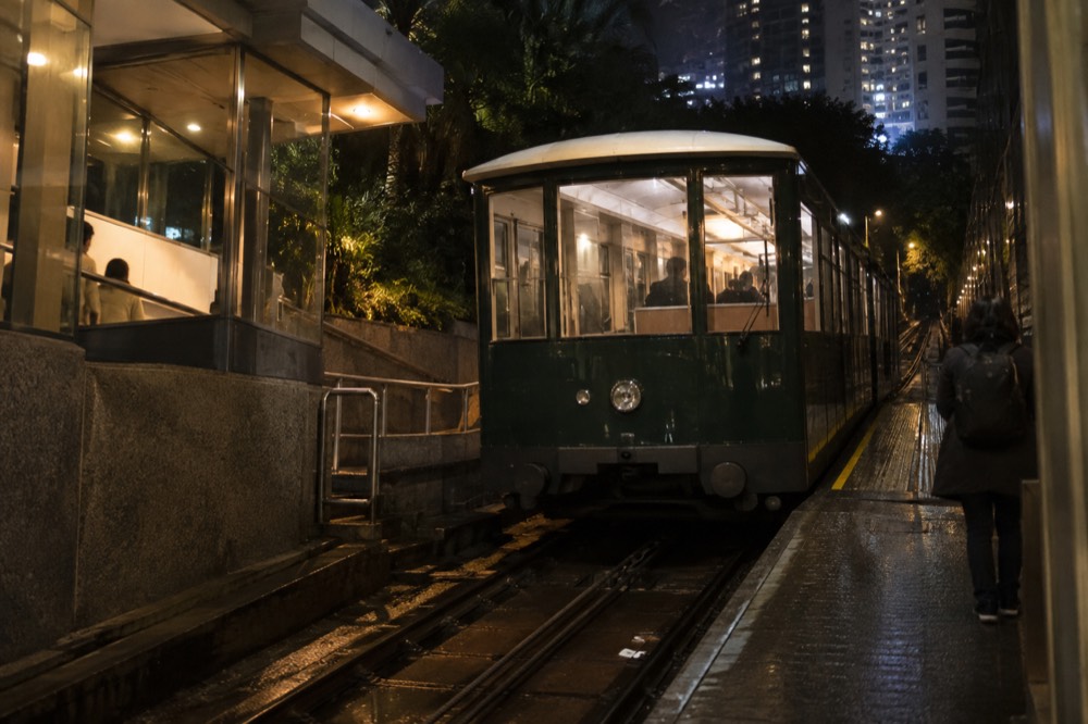 A green funicular tramcar at a hillside station platform in the evening