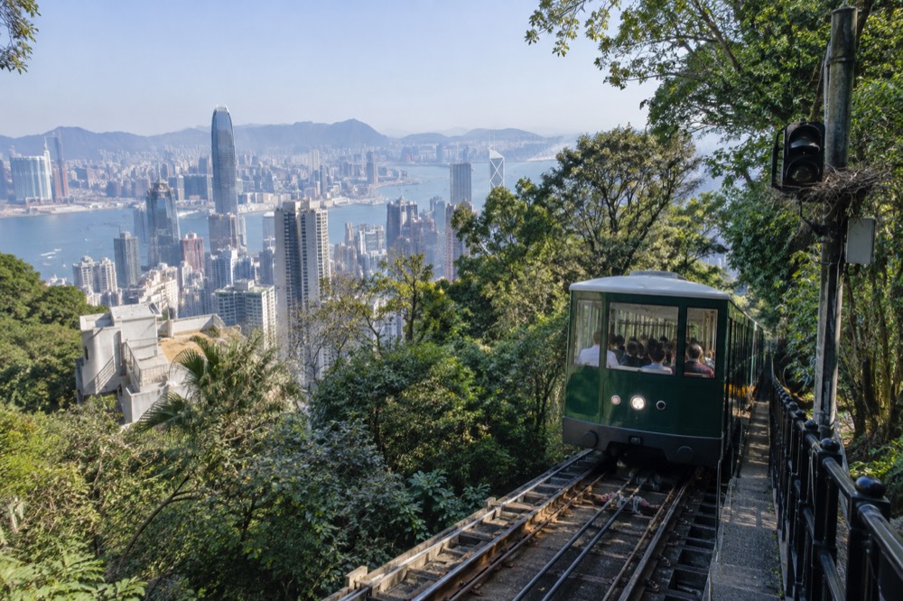Green funicular tramcar climbing the steep track through trees above the city