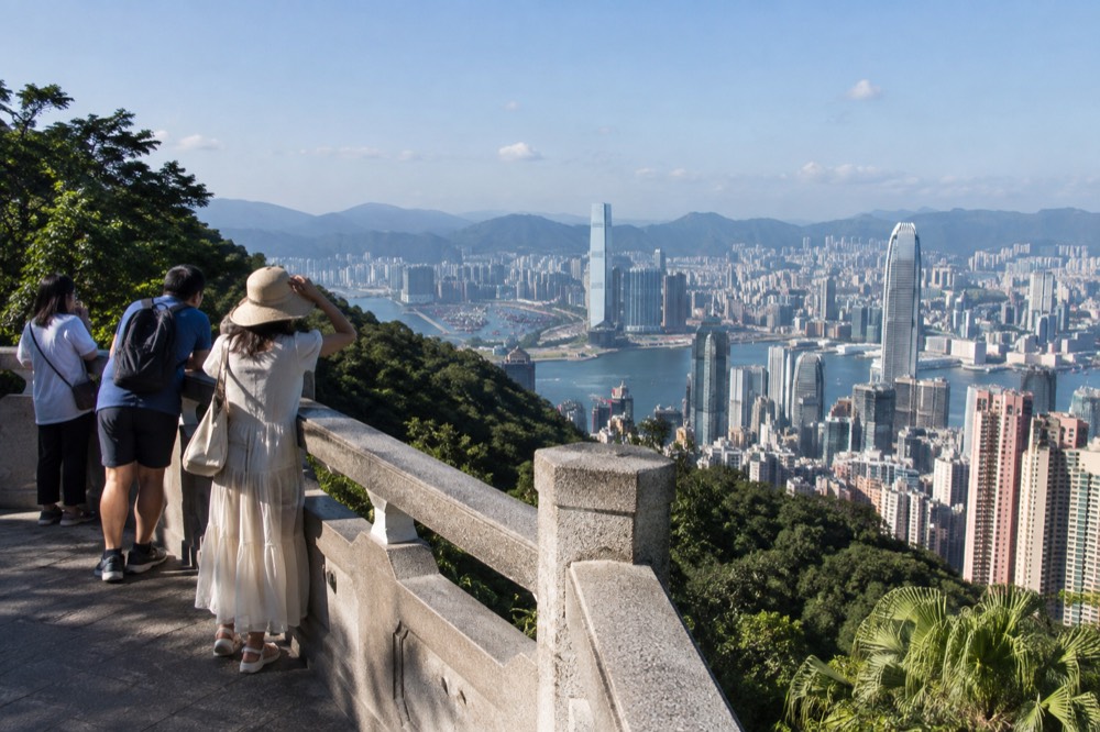 Visitors at an elevated harbour viewpoint looking out over Hong Kong on a bright afternoon