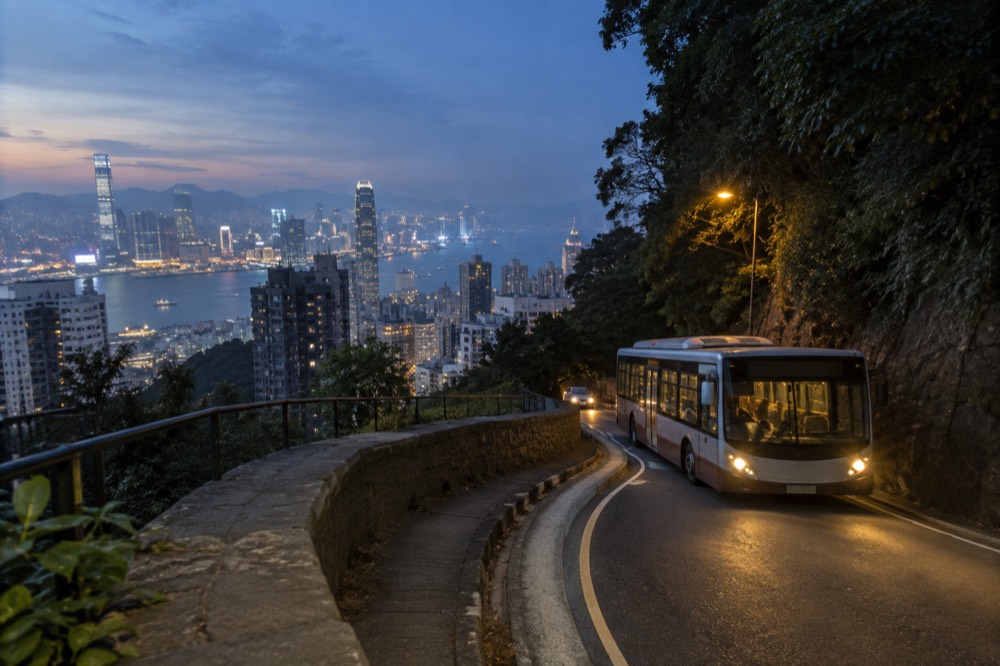 A public bus descending a winding hill road with the city and harbour below