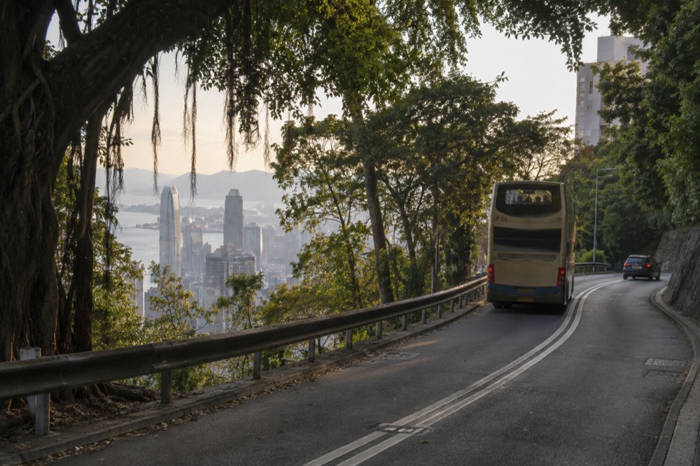 Double-decker bus on the winding road below the Peak with harbour glimpses between trees