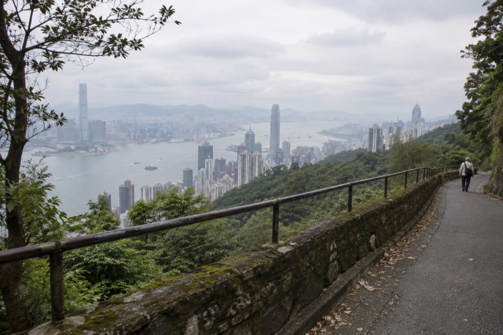 A stone wall and railing along a narrow road with harbour and skyline beyond