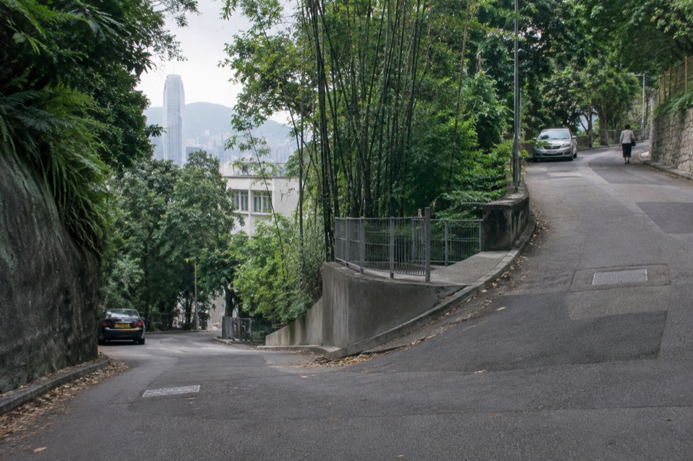 A junction of two narrow hillside roads with trees and a distant tower