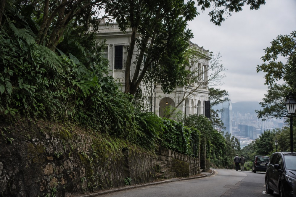An old white historic building behind trees on a narrow hillside road