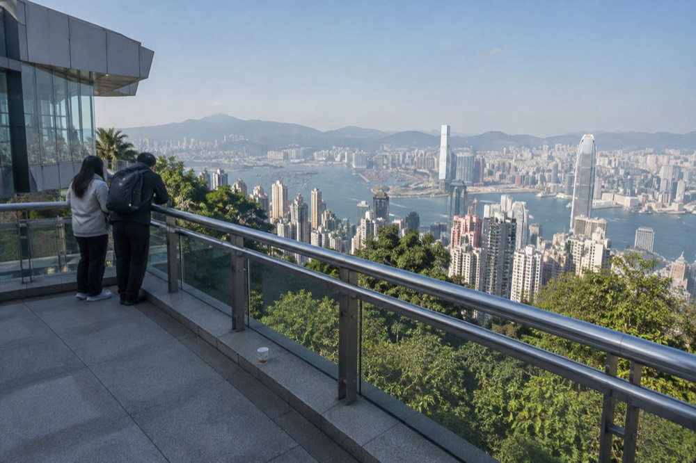 A rooftop viewing deck and harbour skyline seen from a hillside path