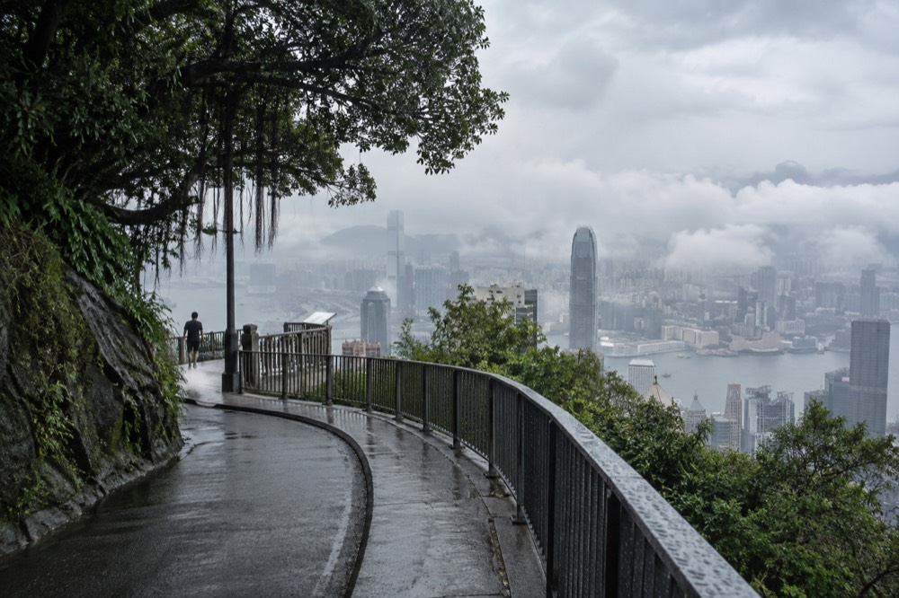 A narrow road with a railing and trees, empty of people, curving along the hillside