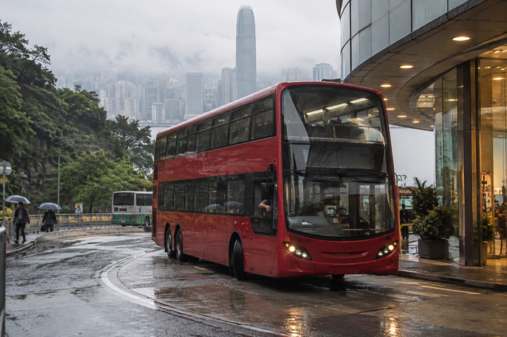 Double-decker bus arriving at a hilltop transport terminus beside a mall building