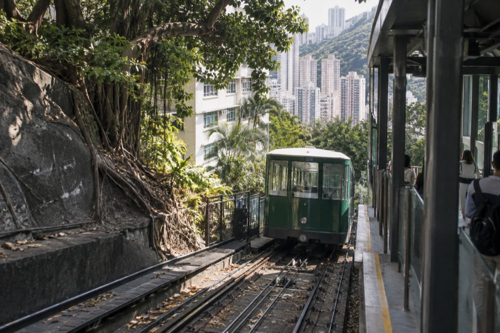 Green funicular tramcar on steep inclined track passing apartment towers on the hillside