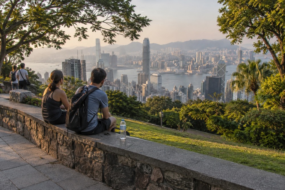 Family and walkers resting on a stone wall above the harbour panorama at the Peak