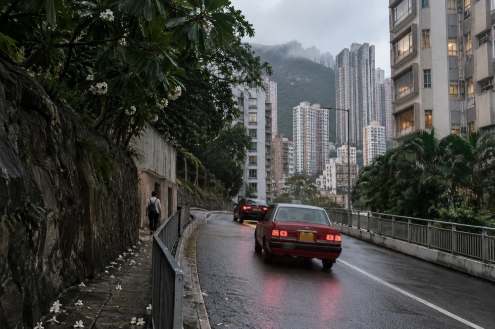 Red Hong Kong taxi on a road with high-rise buildings on both sides