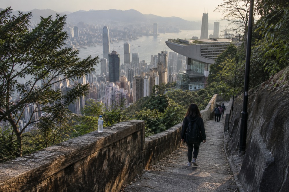 The Peak Tower seen from a nearby path on the hillside, with the harbour and city below