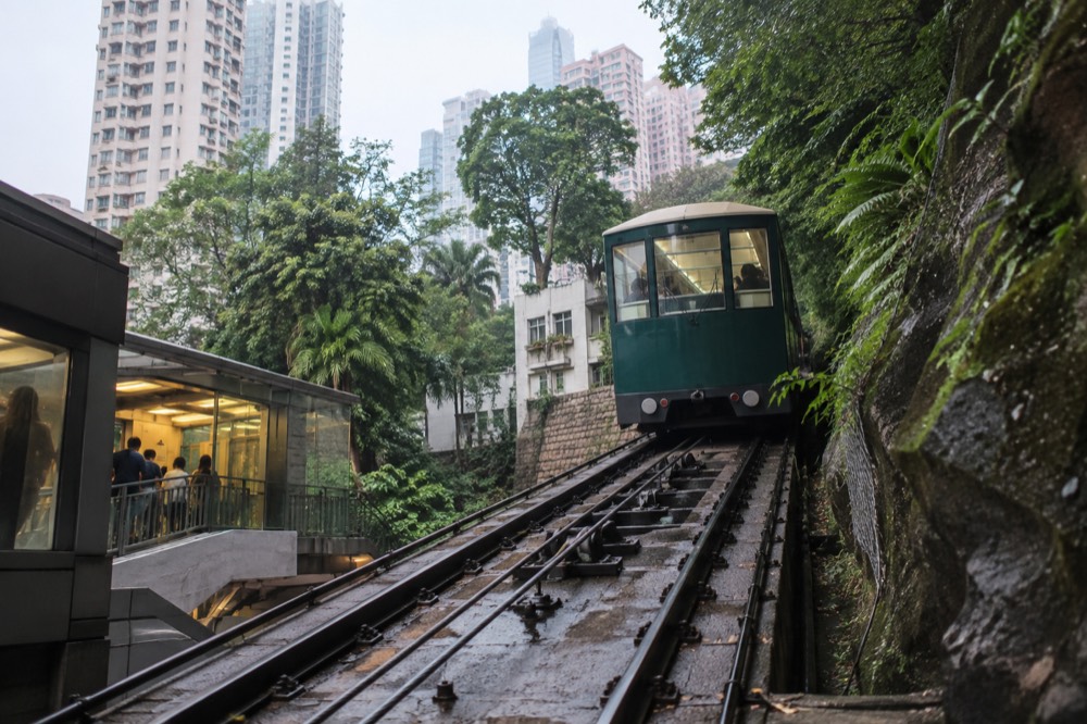 Green Peak Tram car passing apartment towers on a steep forested hillside above Central
