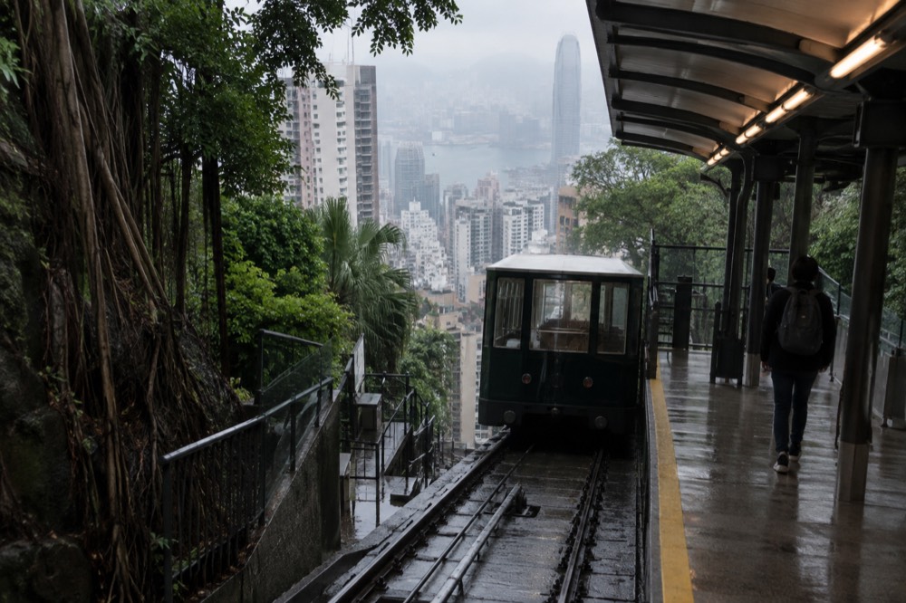 A small hillside funicular station platform beside dense greenery and apartment blocks