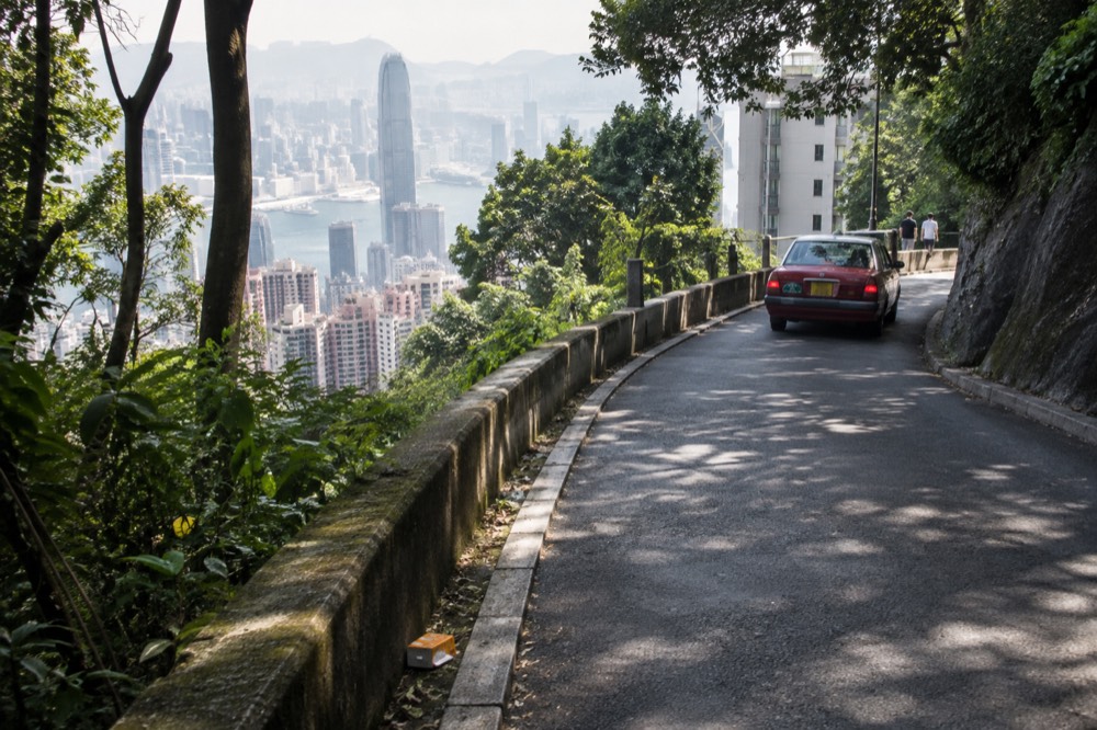 Narrow road curving along a green hillside above apartment blocks