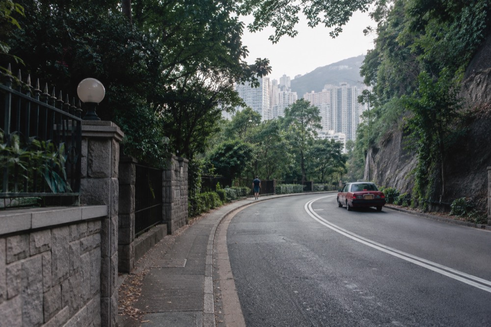 Wide paved road rising through trees on a green hillside