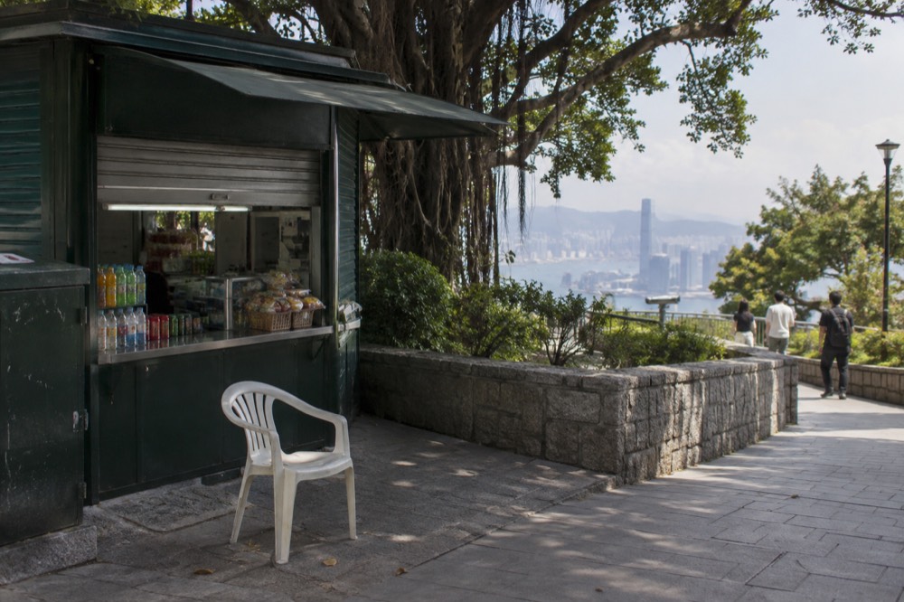 Small refreshment kiosk beside a green park path with trees and low wall