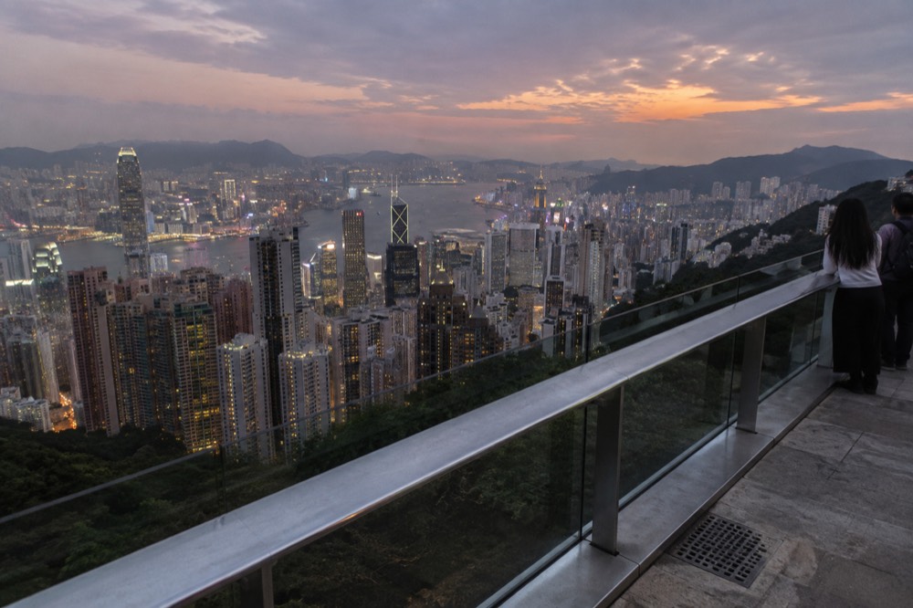 Handheld camera pointed across a harbour skyline at dusk from an elevated walkway